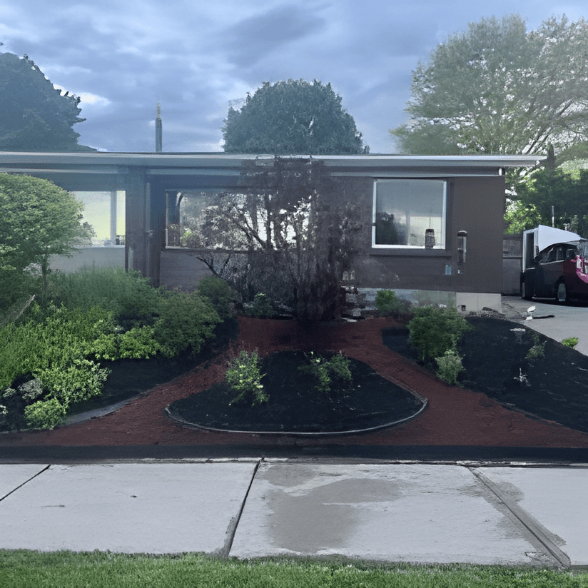Modern brown house with a flat roof and landscaped garden featuring dark mulch and greenery.